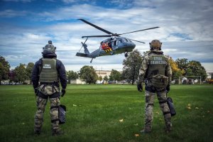 Widok na śmigłowiec Black Hawk w powietrzu zza pleców dwóch funkcjonariuszy Straży Granicznej.