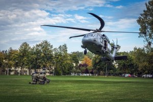 Śmigłowiec Black Hawk podchodzi do lądowania. Na trawiastym lądowisku na wprost helikoptera znajduje się grupa funkcjonariuszy.