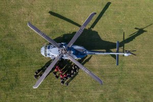 Widok z góry na szary śmigłowiec Black Hawk stojący na trawie w pełnym słońcu. Obok niego znajduje się grupa funkcjonariuszy.