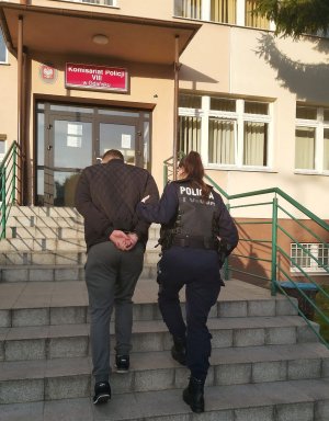 umundurowana policjantka wprowadza po schodach do budynku komisariatu zatrzymanego mężczyznę