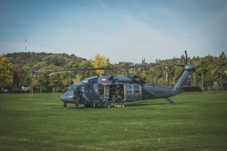 Śmigłowiec Black Hawk na trawiastym lądowisku, po obu stronach dziobu stoją członkowie załogi, w otwartych drzwiach przedziału ładunkowego siedzą dwaj policyjni kontrterroryści.