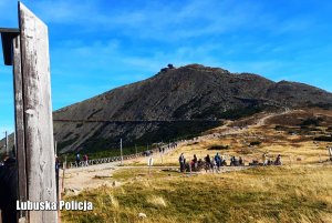 Widok na Śnieżkę i na szlak górski, którym idą turyści, a inni z boku odpoczywają