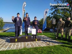 Podium na którym stoją policjantki nagrodzone w biegu, po prawej stronie stoją żołnierze którzy wręczali nagrody. W tle jezioro