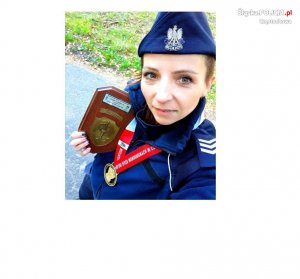 umundurowana policjantka z medalem na szyi i pamiątkowa tabliczka w ręce