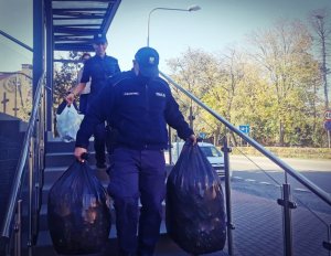 Policjanci schodzą ze schodów. Mają w rękach worki z nakrętkami