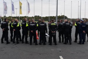 policjanci oraz żołnierze żandarmerii wojskowej stoją w grupie, w tle maszty z flagami