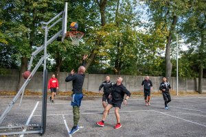 sześciu mężczyzn na boisku do gry w streetball. Jeden  z nich rzuca piłkę do kosza