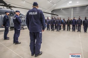wnętrze hangaru grupa policyjnych lotników stoi naprzeciwko  trzech policjantów, wśród których jest Komendant Główny Policji