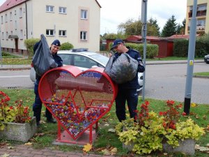 dwoje  umundurowanych policjantów wrzuca nakrętki do ustawionego serca. w tle widać policyjny radiowóz