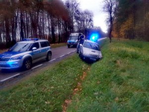 Miejsce kolizji drogowej. Kia typu van znajduje się w rowie. Na drodze stoją dwa policyjne radiowozy