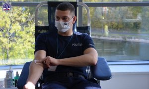 policjant w koszulce polo siedzi na fotelu i trzyma wacik w miejscu, z którego miał pobieraną krew