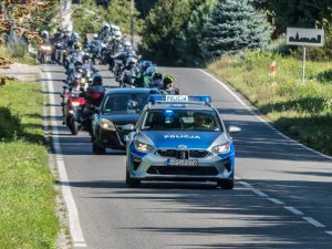 na pierwszym planie radiowóz  policyjny jadący drogą, za nim jedzie samochód osobowy oraz grupa motocyklistów na motocyklach