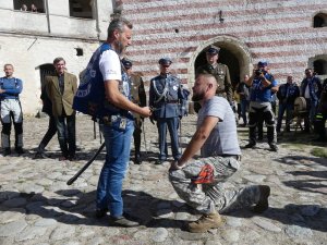 pasowanie na członka klubu, mężczyzna klęczy na jednym kolanie, a drugi stoi przed i szablą dotyka jego ramienia