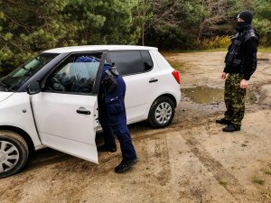 umundurowany policjant sprawdza białe auto, za samochodem stoi funkcjonariusz straży granicznej