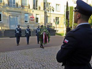 Złożenie wieńca przed obeliskiem &quot;Poległym Policjantom - Rzeczpospolita Polska&quot; na dziedzińcu Komendy Głównej Policji. Na pierwszym planie funkcjonariusz trzymający wartę honorową, w tle komendanci i budynek KGP.