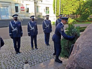 Moment złożenia wieńca przed obeliskiem &quot;Poległym Policjantom - Rzeczpospolita Polska&quot; przez funkcjonariusza z kompanii reprezentacyjnej. W tle komendanci i budynek Komendy Głównej Policji.