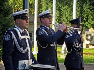 Hejnalista z Orkiestry Reprezentacyjnej Policji wraz z dwoma funkcjonariuszami kompanii reprezentacyjnej przed budynkiem Komendy Głównej Policji.