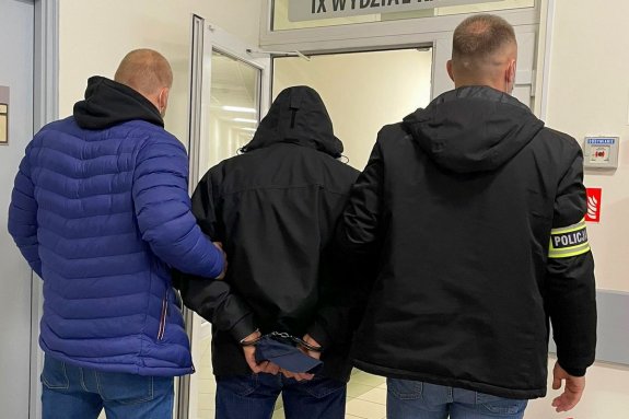 dwaj nieumundurowani policjanci prowadzą zatrzymanego skutego kajdankami