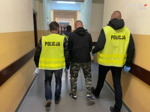 dwaj policjanci w żółtych kamizelkach prowadzą zatrzymanego mężczyznę - widok z tyłu