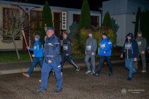 pora nocna, mężczyźni i kobiety w strojach sportowych maszerują, na czele idzie umundurowany policjant