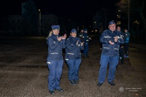 pora nocna, dwie umundurowane policjantki i policjant klaskają, w tle inni policjanci