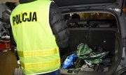 Policjant w żółtej kamizelce z napisem policja zagląda do bagażnika samochodu