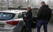 zatrzymana kobieta z policjantem stoi przed nieoznakowanym radiowozem