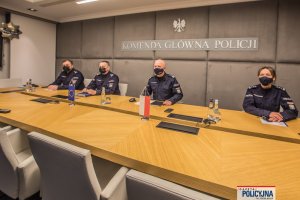 trzej umundurowani oficerowie i policjantka oficer siedzą za stołem w sali konferencyjnej,za nimi widoczny jest napis Komenda Główna Policji
