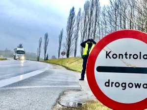 Droga, znak kontrola drogowa, w tle policjant, obserwujący przez lornetkę