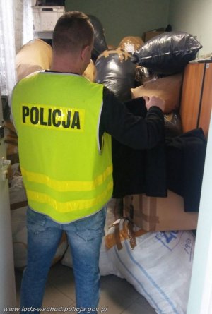 policjant w żółtej kamizelce z napisem policja ogląda zabezpieczony towar spakowany w worki foliowe