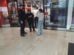 dwaj policjanci kontrolują kobietę, w tle witryna sklepowa w galerii handlowej