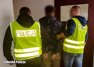 policjanci ubrani w żółte kamizelki z napisem Policja prowadzą zatrzymanego mężczyznę