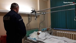 policjant stoi w sali szpitalnej nad łóżkiem sprawcy wypadku