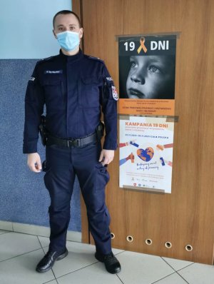 policjant stoi na korytarzu na tle drzwi, na których wisi plakat