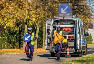 policjanci wystawiają znaki drogowe oznaczające wypadek, w tle ambulans pogotowia ruchu drogowego