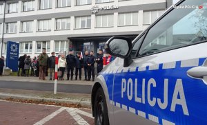 radiowóz policyjny i grupa osób stojących przed budynkiem komendy