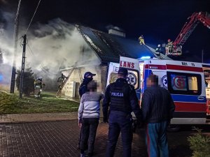 Policjanci wraz z ewakuowanymi mieszkańcami stoją przy karetce
