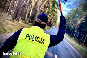 policjant w żółtej kamizelce z napisem Policja zatrzymuje nadjeżdżający pojazd