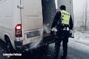 policjant w żółtej kamizelce z napisem sprawdza wnętrze pojazdu