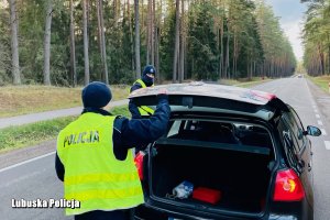 policjant w żółtej kamizelce z napisem Policja sprawdza bagażnik pojazdu
