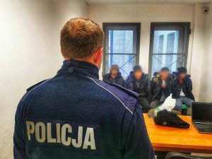 umundurowany policjant stojący przed imigrantami