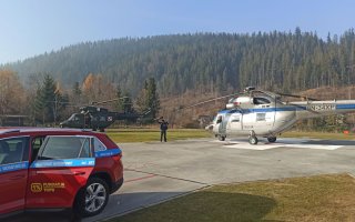 Samochód TOPR na pierwszym planie, na drugim planie śmigłowiec policyjny oraz wojskowy.