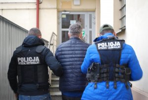 dwaj policjanci w kamizelkach z napisem Policja wydział kryminalny prowadzą zatrzymanego