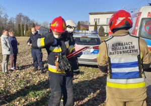 grupa strażaków, z  tyłu stoi dzielnicowy i dwie kobiety