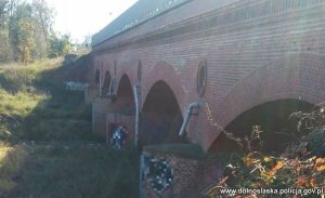 widok wiaduktu kolejowego na filarach ceglanych którego narysowane są dwa graffiti zasłonięte cenzurą