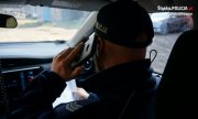Na zdjęciu policjant wewnątrz radiowozu, podczas prowadzenia rozmowy telefonicznej na temat stanu zdrowia z osoba objętą kwarantanną domową