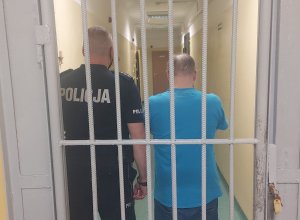 policjant z zatrzymanym stoją za kratą