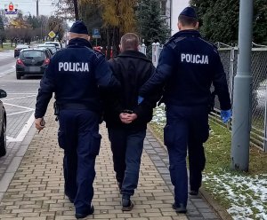 Zatrzymany 61-latek w kajdankach prowadzony przez dwóch umundurowanych policjantów