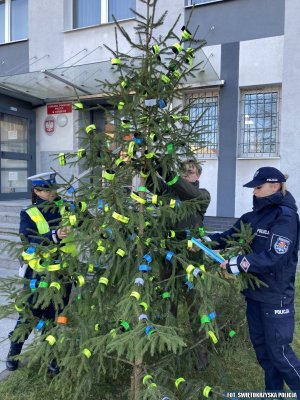 policjanci wspólnie z przedstawicielem z Nadleśnictwa Barycz ubierają choinkę w odblaskowe opaski