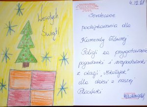 Przygotowana przez dzieci kartka świąteczna, którą otrzymały policjantki w czasie wizyty. Na pierwszej stronie widać dziecięcy rysunek – choinkę z czerwonymi bombkami i czerwono-pomarańczowy prezent oraz napis „Wesołych Świąt!” na żółtym tle z niebieskimi śnieżynkami. Wewnątrz kartki na białym tle napisano: „Serdeczne podziękowania dla Komendy Głównej Policji za przygotowanie pogadanki i niespodzianki z okazji ‘Mikołajek’ dla dzieci z naszej Placówki.”